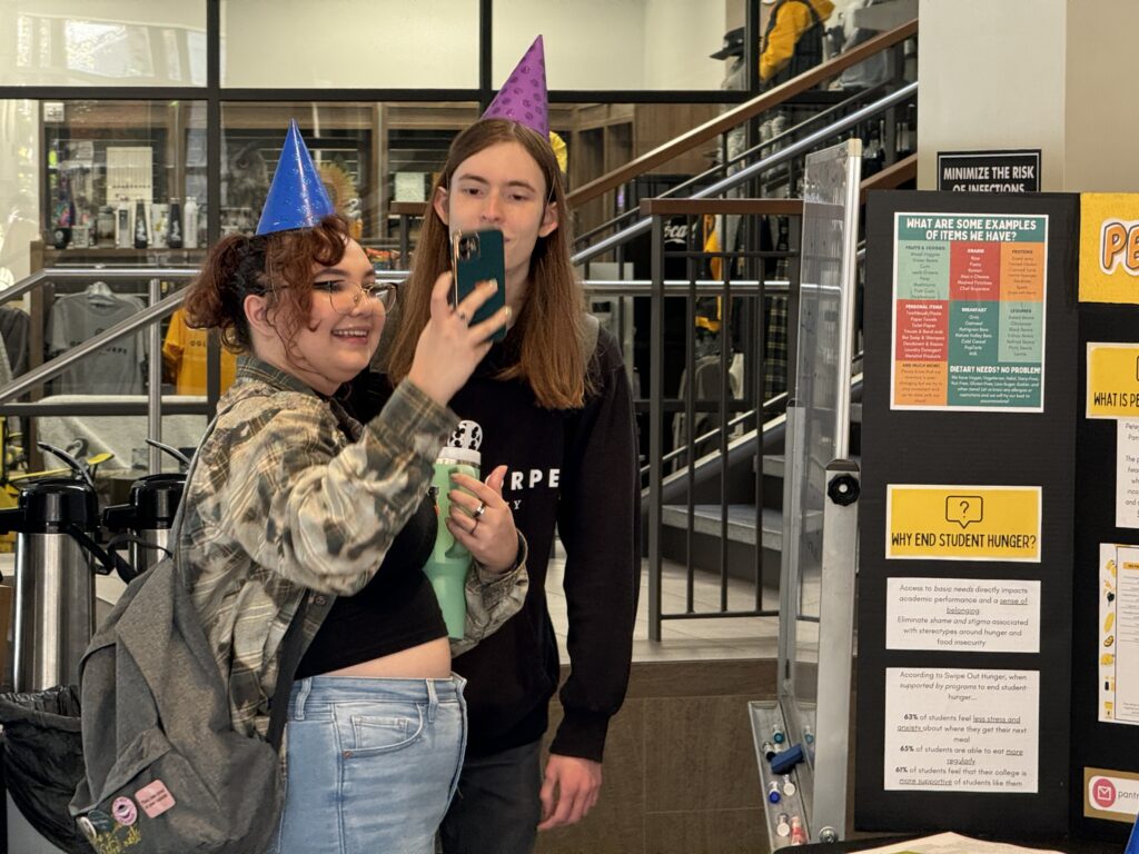 Two students wearing party hats taking a selfie at the "Petey's Pantry Two-Year Celebration."