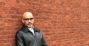 Headshot of poet Willie Perdomo standing in front of a brick wall