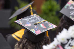 Decorated graduation cap with two butterflies-- one with the US flag as wings and the other with the Mexican flag on its wings. A drawing of a Latina graduate sitting on a half globe-half brain is at the bottom of the cap. The quote on the cap reads "Si puedes cambiar tu mente puedes cambiar el mundo. Gracias mamá y papá." Translated "If you can change your mind, you can change the world. Thank you mom and dad."