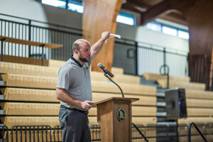 Man gestures at a podium in gymnasium