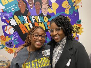 Two women pose with a colorful mural in the background