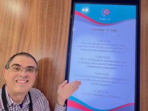 Dr. John Nardo in front of a large itinerary pointing to his workshop session